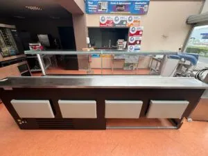 Comptoir réfrigéré professionnel, structure noire avec plateau inox et pare-haleine en verre, vu de l’arrière.