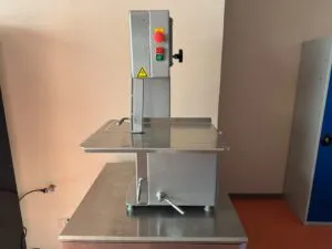 Scie à os professionnelle en inox, vue latérale, posée sur un plan de travail.