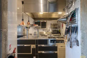 Îlot de cuisson professionnel noir et inox avec plaques et tiroirs réfrigérés, installé sous hotte en cuisine carrelée.