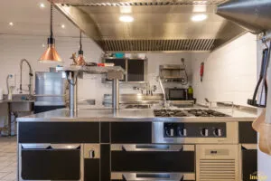 Îlot de cuisson professionnel noir et inox avec plaques et tiroirs réfrigérés, installé sous hotte en cuisine carrelée.