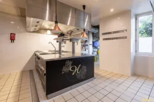 Îlot de cuisson professionnel noir et inox avec plaques et tiroirs réfrigérés, installé sous hotte en cuisine carrelée.