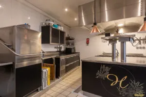 Îlot de cuisson professionnel noir et inox avec plaques et tiroirs réfrigérés, installé sous hotte en cuisine carrelée.