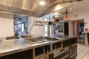 Îlot de cuisson professionnel noir et inox avec plaques et tiroirs réfrigérés, installé sous hotte en cuisine carrelée.