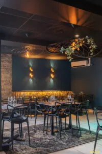 Banquette dorée capitonnée sous mur bleu avec deux appliques design allumées, table dressée et verres à vin au premier plan.