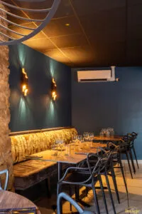 Banquette dorée capitonnée sous mur bleu avec deux appliques design allumées, table dressée et verres à vin au premier plan.