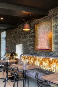 Banquette dorée capitonnée sous mur bleu avec deux appliques design allumées, table dressée et verres à vin au premier plan.