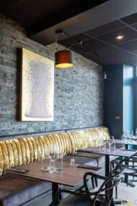 Banquette dorée capitonnée sous mur bleu avec deux appliques design allumées, table dressée et verres à vin au premier plan.