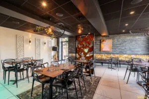 Salle de restaurant moderne avec tables dressées, chaises noires design et banquettes dorées sous éclairage tamisé.