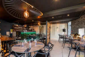 Salle de restaurant moderne avec tables dressées, chaises noires design et banquettes dorées sous éclairage tamisé.