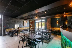 Salle de restaurant moderne avec tables dressées, chaises noires design et banquettes dorées sous éclairage tamisé.