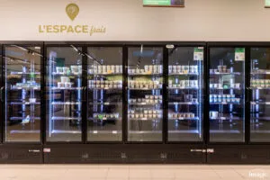Vitrines réfrigérées vitrées pleines de produits frais sous l’enseigne « L’Espace frais » dans un rayon de magasin.