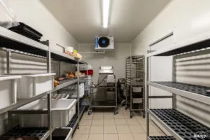 Chambre froide équipée de rayonnages inox remplis de bacs et produits, évaporateur au plafond et matériel de préparation mobile au fond