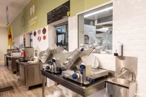 Deux trancheuses en inox à poignées bleues sur plan de travail, évier intégré à droite dans un comptoir de produits frais