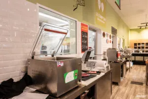 Machine sous-vide à cloche en inox, couvercle relevé, posée sur un plan de travail dans un comptoir de produits frais.
